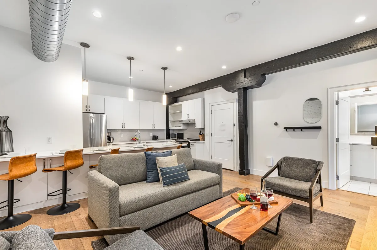 A spacious and welcoming open-concept living area featuring a comfortable sofa, coffee table, bar stools, and a kitchen counter—ideal for socializing, late-night snacks, or winding down after a night out.