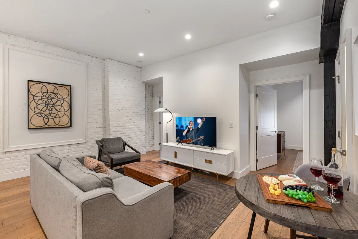 A cozy living room featuring a soft sofa, a modern coffee table, a large television mounted on the wall, and colorful artwork. The space feels inviting and is set up for group activities like watching TV, sharing snacks, or having intimate conversations.