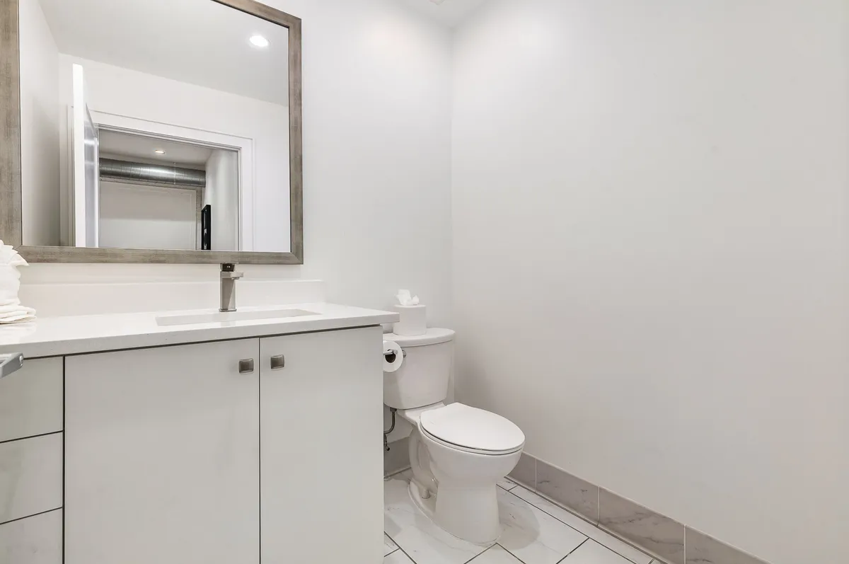 A sleek, modern powder room featuring a vanity with a sink, large mirror, toilet, and neatly arranged towels. The minimalist style and fresh presentation make it ideal for quick refreshes or personal grooming, mirroring the convenience of having additional half baths.