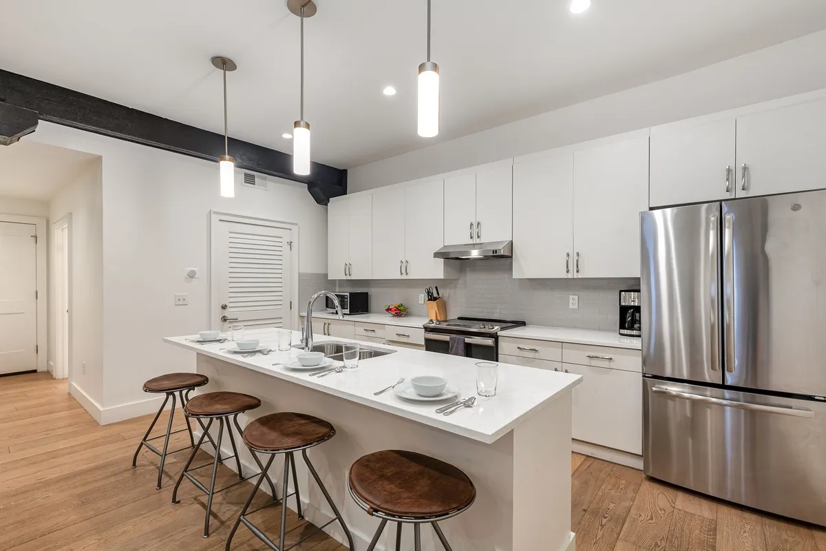 A welcoming kitchen scene with an island countertop, sleek stainless steel appliances, and stylish hanging light fixtures. The island offers plenty of space for meal prep or casual dining, with bar stools inviting guests to gather and interact.