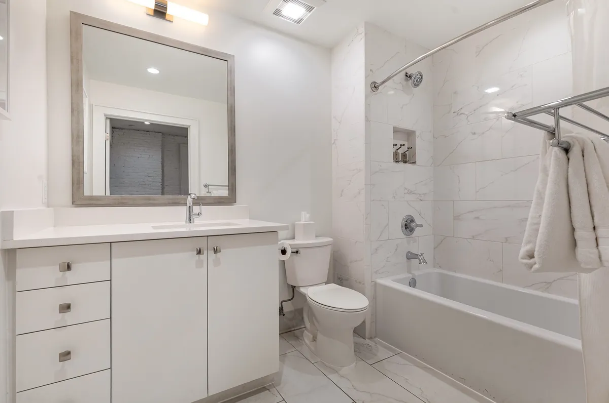 A spacious bathroom with a large mirror, modern vanity, and inviting bathtub. The setting is light-filled and exudes a calm, refreshing vibe, emphasizing the spa-inspired atmosphere and comfort described in the text.